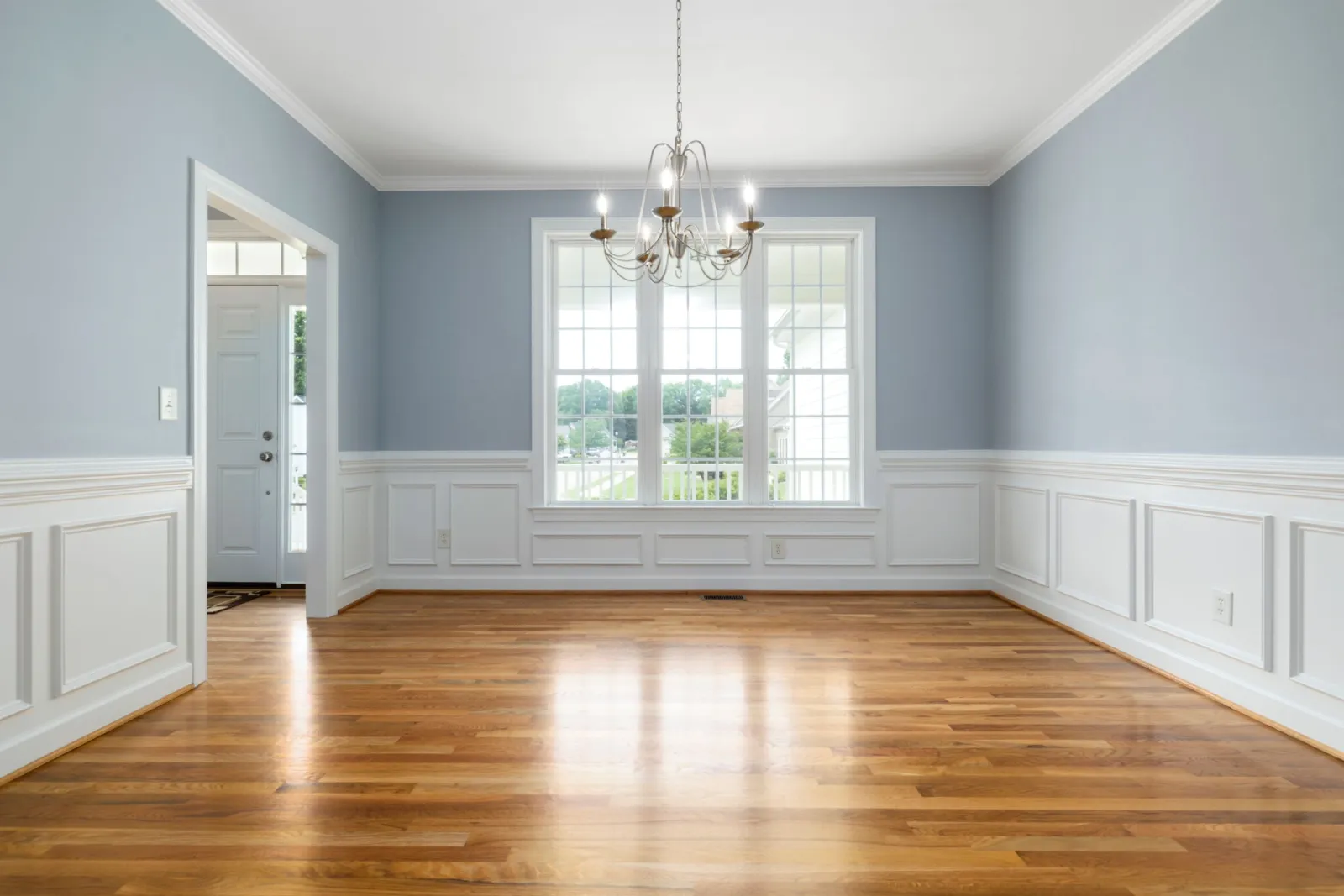 Sunlit white oak hardwood flooring in a bright DMV living room with raised-panel wainscoting and a bay window, installed by F&F Surface Group
